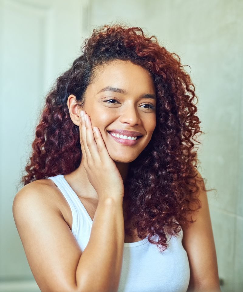 A woman with clear acne-free skin looking into the mirror smiling and happy that her acne is now gone.