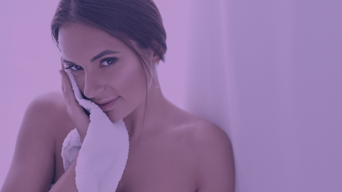 A woman with dry skin smiling and using a towel to dry her face.