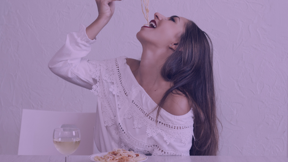 A woman enjoying a plate of pasta which are one of the foods listed as food to avoid (carbs) if you have oily and acne prone skin.