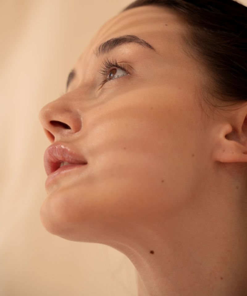 A side portrait of a woman with dry skin with soft lighting on her face presumably looking into a mirror. 